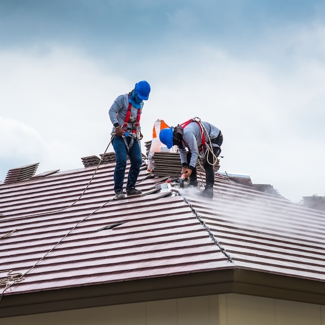 Two roofers are shaping roofing tiles for the slope of the roof.