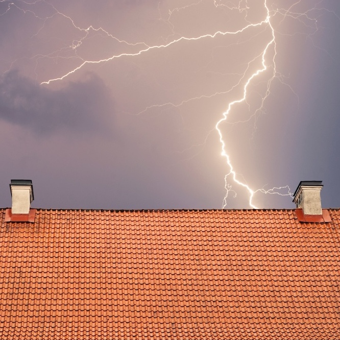 A tile roof is seen with a streak of lightning in a cloudy grey sky