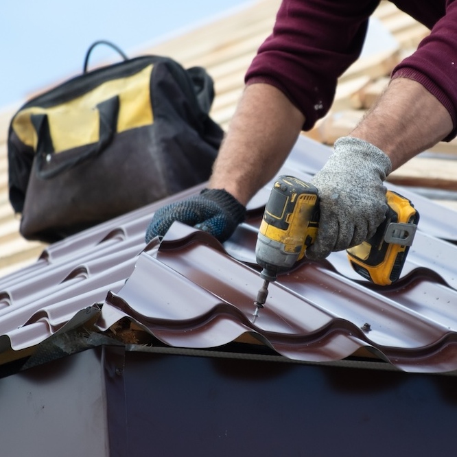 A roofer is skillfully drilling a hole in a metal roof shingle.