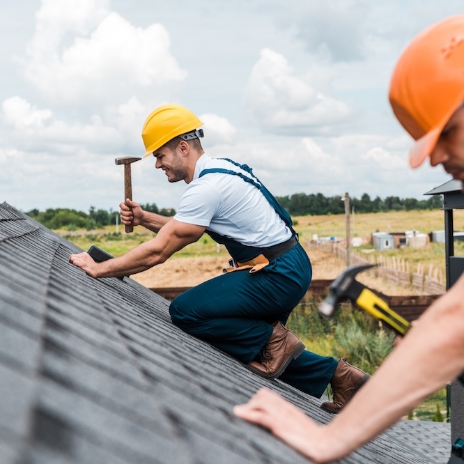 A roofer is hammering in nails.