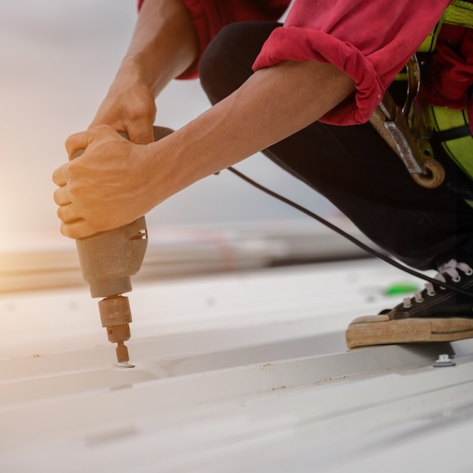 A roofer is drilling a new metal panel into place.