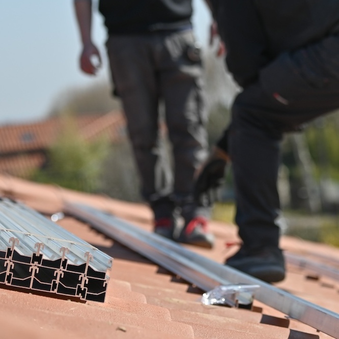 Two roofers are working on a roof system in its early stages.