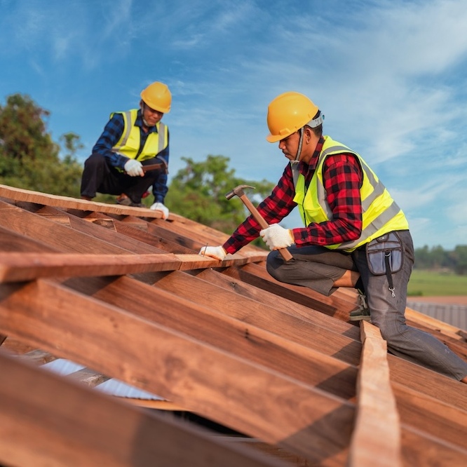 Two roofers are hammering nails into a fresh roof system.